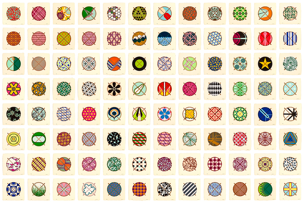 96 small, colorful, framed square papers with circle-shaped wood-block prints in white square frames hang in a large grid on the wall. Each circle has a thin brown border and two brown lines that extend beyond the circle to form an X through its center. The circles are filled with vibrant geometric patterns and flattened imagery, including flowers, grass, stars, and checkerboards. Each design within the circles is unique.